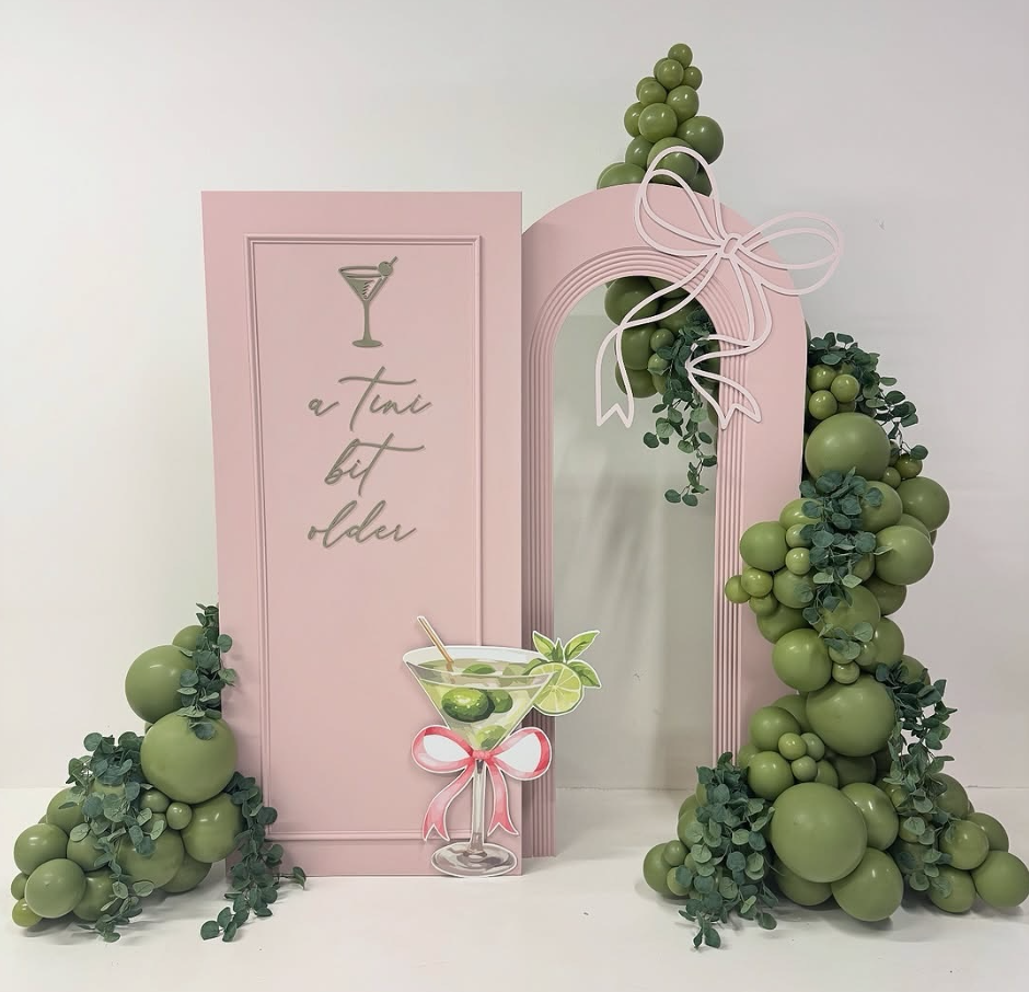 Pink cocktail themed backdrop with green balloon garland
